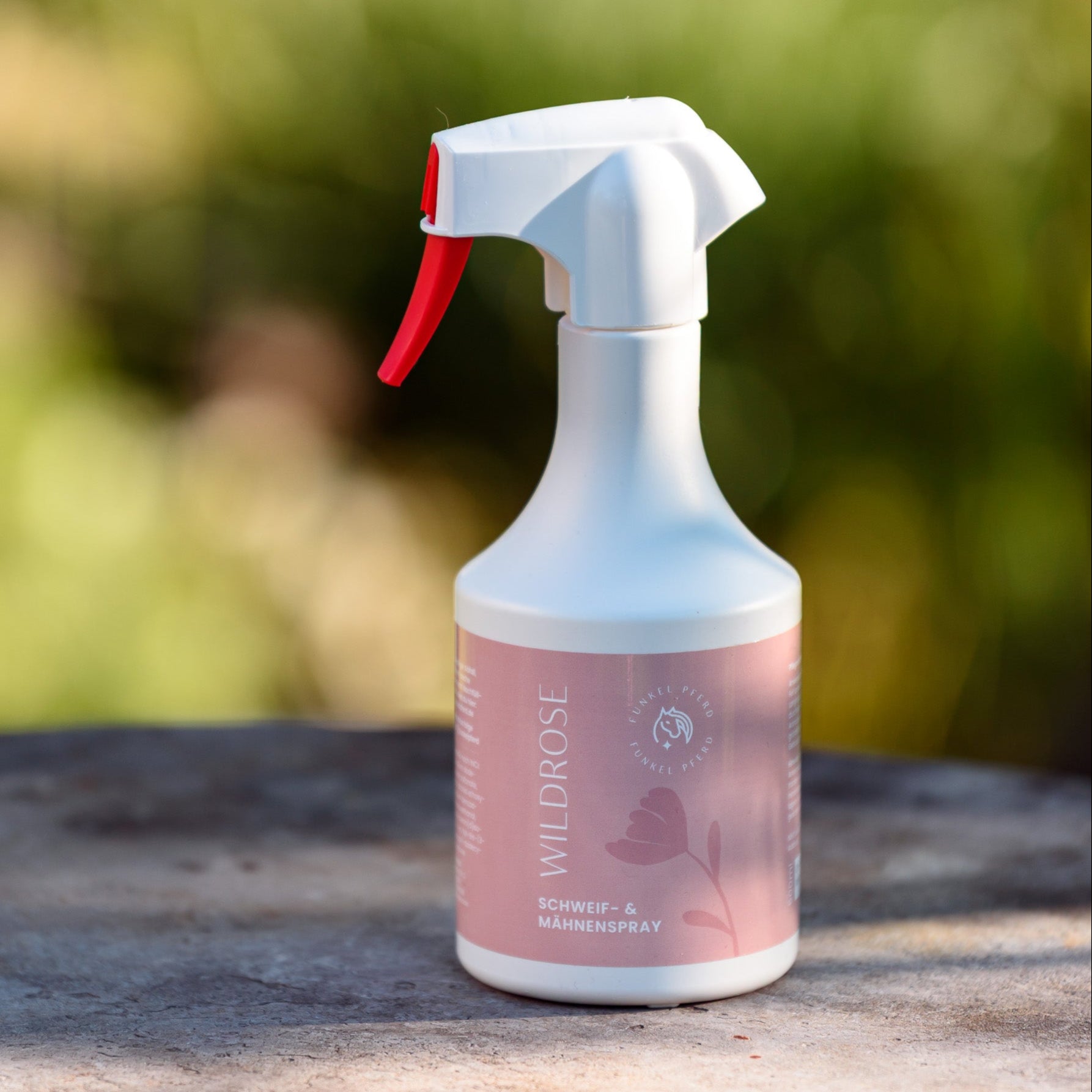 Sprühflasche Schweif- und Mähnenspray mit Wildrosenduft mit rosa Etikett mit Illustration einer Rose vor natürlichem Hintergrund